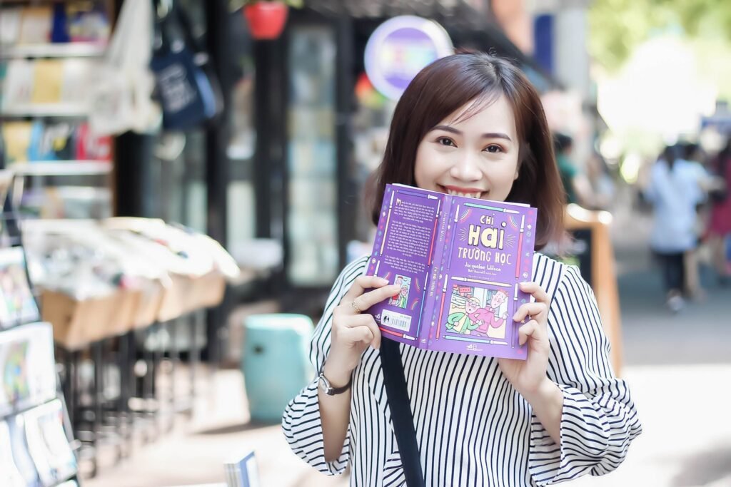Cheerful woman reading a book in a vibrant outdoor setting, enjoying a sunny day in the city.